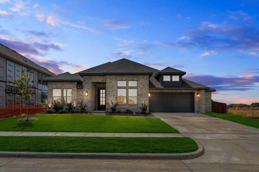Single-story brick home with dark roof, two-car garage, and manicured front lawn at dusk