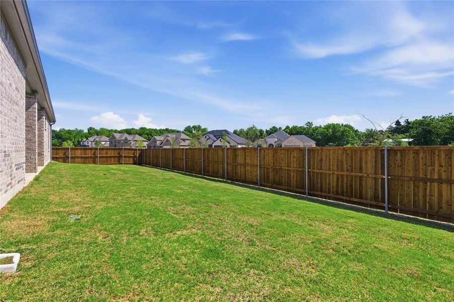 Expansive green lawn featuring a wood privacy fence and a brick-sided exterior