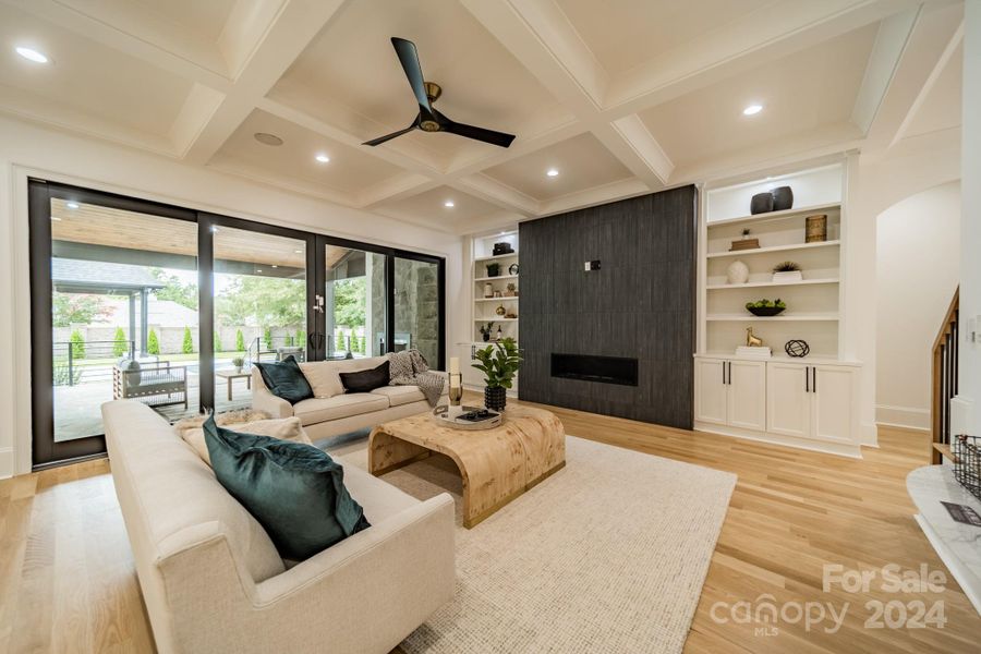 Family room with accent TV wall, built-in storage and folding glass doors leading to covered patio with fireplace