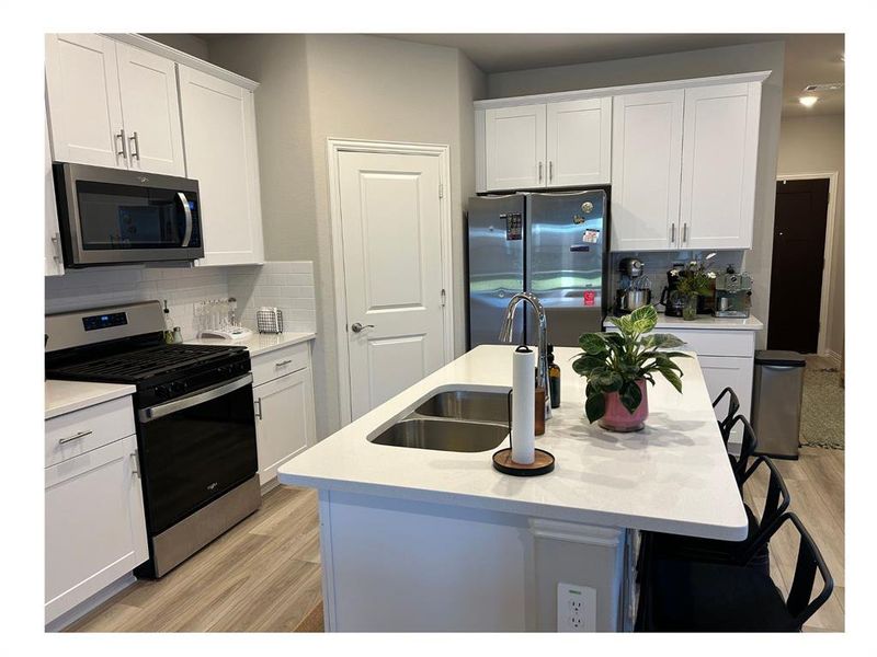 Kitchen featuring light hardwood / wood-style flooring, backsplash, an island with sink, white cabinets, and appliances with stainless steel finishes