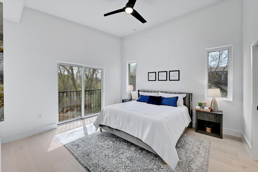 Bedroom featuring  ceiling fan, access to exterior, light wood-style floors, and a towering ceiling