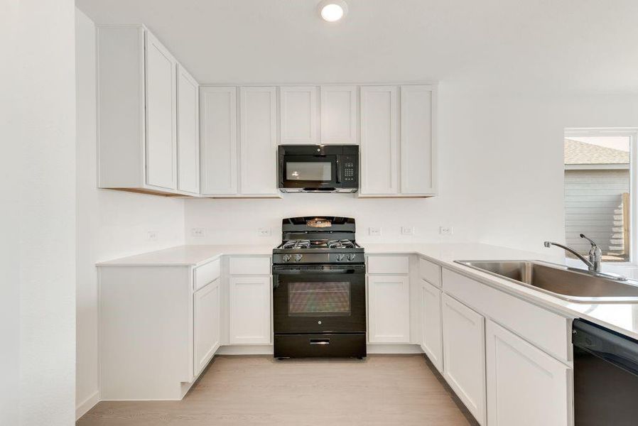 Kitchen featuring black appliances, a sink, light countertops, and white cabinets