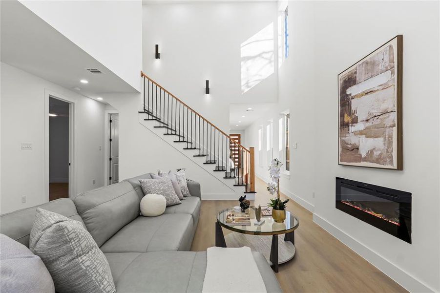 Living room with a high ceiling, a glass covered fireplace, stairs, wood finished floors, and recessed lighting