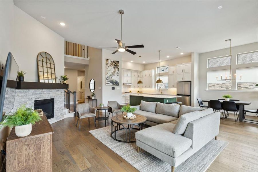 Living room with light hardwood / wood-style flooring, ceiling fan with notable chandelier, and a stone fireplace