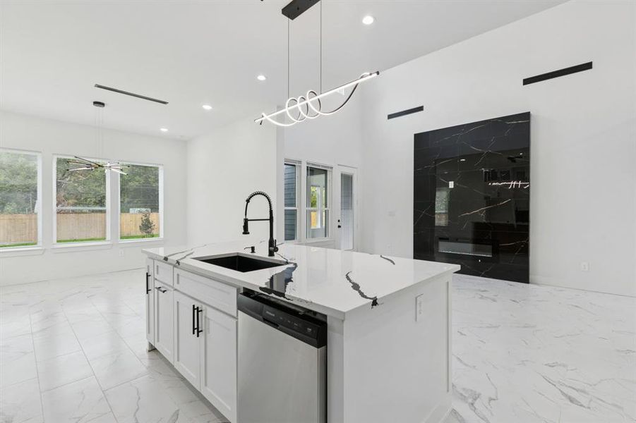 Kitchen featuring white cabinetry, decorative light fixtures, dishwasher, a kitchen island with sink, and light marble finish flooring Kitchen featuring white cabinetry, decorative light fixtures, dishwasher, a kitchen island with sink, and light marble finish flooring