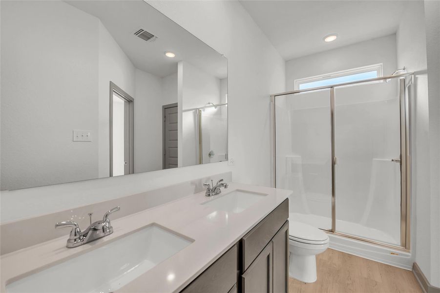 Bathroom featuring double vanity, a shower stall, light wood finished floors, and recessed lighting