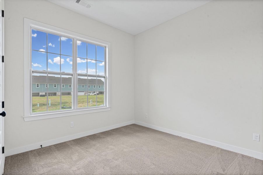 Bright room featuring a large gridded window, white trim, light-colored walls, and neutral carpet flooring Bright room featuring a large gridded window, white trim, light-colored walls, and neutral carpet flooring