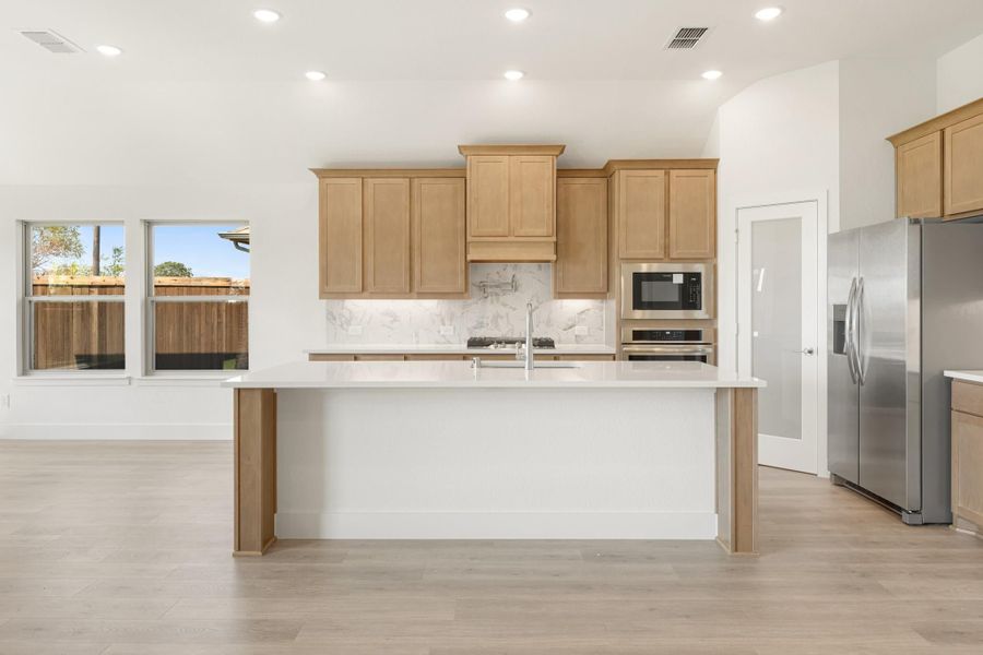 Kitchen with large center island, light wood cabinets, marble backsplash, and stainless steel appliances