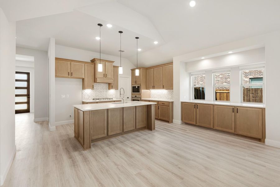 Open kitchen with light wood cabinets, center island, pendant lights, and vaulted ceiling over light hardwood floors