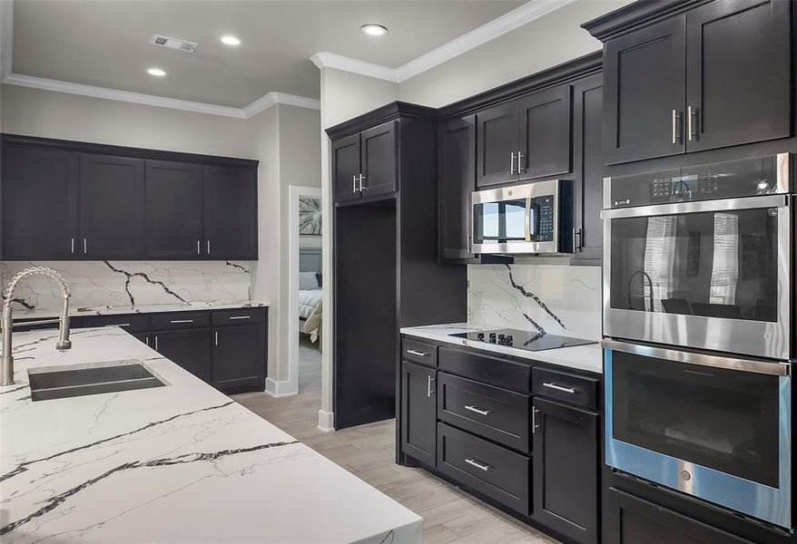 Kitchen featuring stainless steel appliances, light stone counters, tasteful backsplash, dark cabinetry, and crown molding