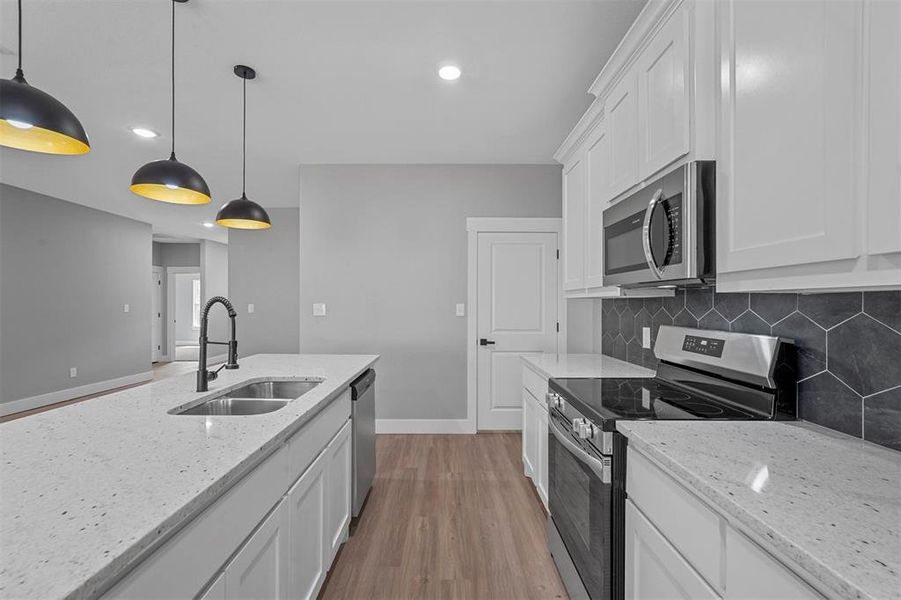 Kitchen with hanging light fixtures, stainless steel appliances, light hardwood / wood-style floors, white cabinetry, and sink