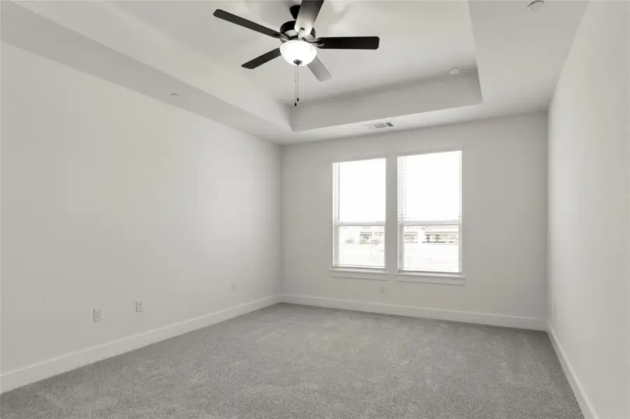 Spare room with a raised ceiling, light colored carpet, and a ceiling fan