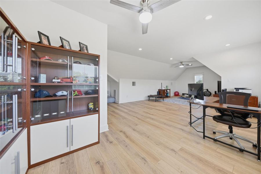 A versatile open loft with warm wood flooring and bright recessed lighting offers abundant natural light.
