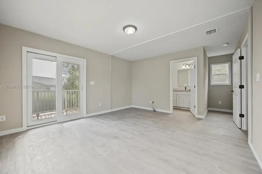Neutral wall-toned room featuring wood-finish flooring, white sliding glass door, flush-mount ceiling lighting, and crisp white trim Neutral wall-toned room featuring wood-finish flooring, white sliding glass door, flush-mount ceiling lighting, and crisp white trim