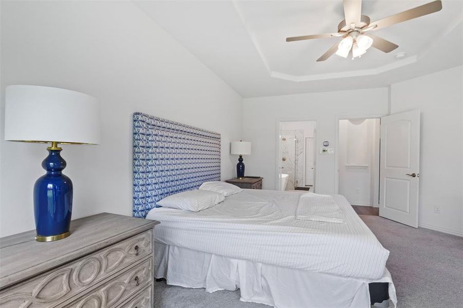 Carpeted bedroom with a tray ceiling, a ceiling fan, and ensuite bath