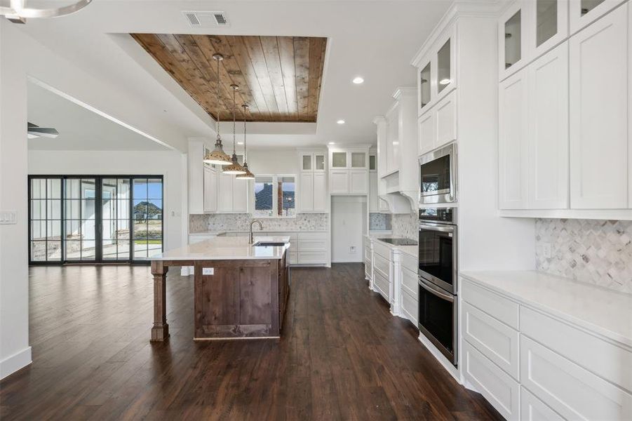 Kitchen with stainless steel microwave, a kitchen island with sink, white cabinets, tasteful backsplash, and dark hardwood / wood-style flooring