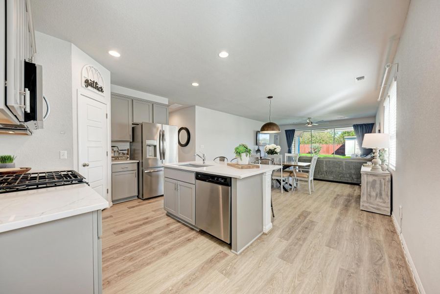 Kitchen with gray cabinetry, open floor plan, an island with sink, decorative light fixtures, and appliances with stainless steel finishes