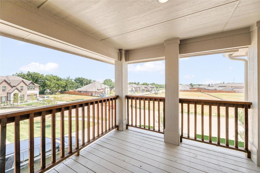 Covered second-floor balcony with wood railing and neighborhood views on a sunny day Covered second-floor balcony with wood railing and neighborhood views on a sunny day