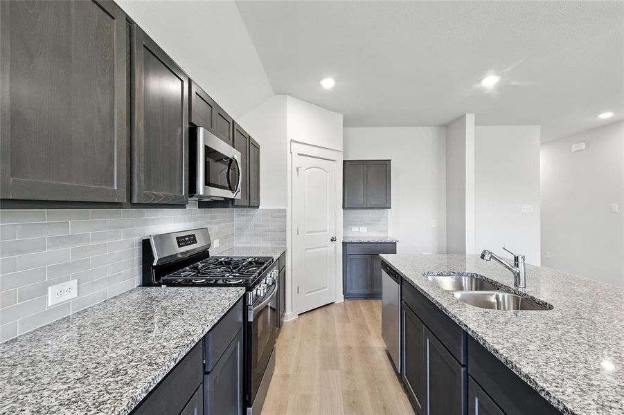 Kitchen with stainless steel appliances, light wood finished floors, light stone countertops, tasteful backsplash, and recessed lighting