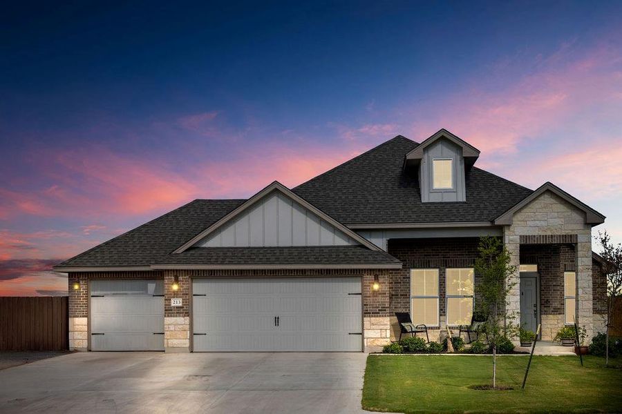 View of front of home with stone siding, roof with shingles, a garage, and brick siding