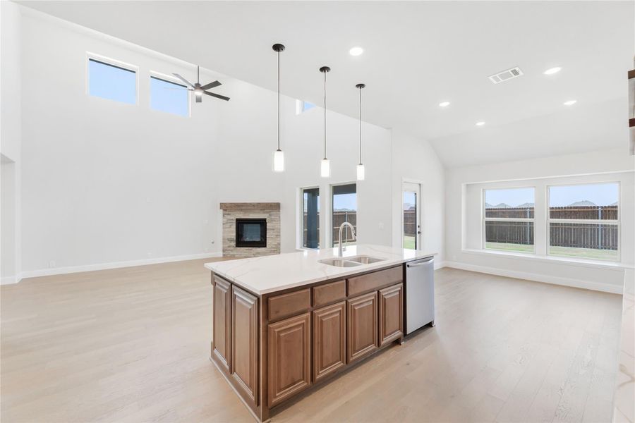 Open-concept kitchen with wood island, pendant lights, vaulted ceiling, and stone fireplace in background Open-concept kitchen with wood island, pendant lights, vaulted ceiling, and stone fireplace in background