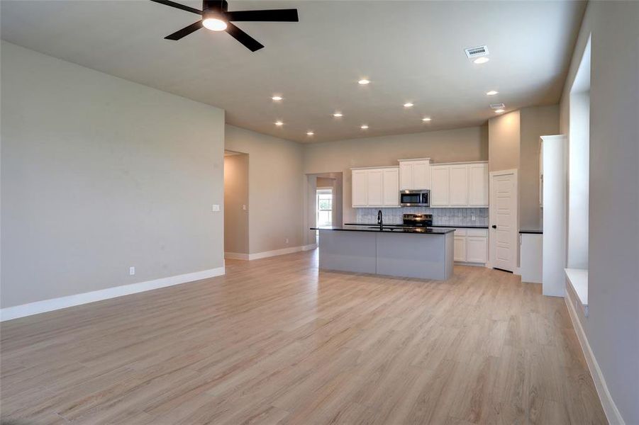 Kitchen featuring dark countertops, open floor plan, white cabinetry, tasteful backsplash, and light wood-style floors Kitchen featuring dark countertops, open floor plan, white cabinetry, tasteful backsplash, and light wood-style floors