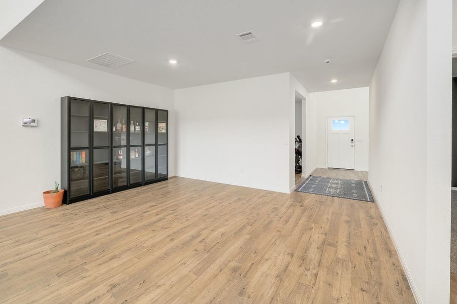 Open-concept living area with wood-finish flooring, recessed lighting, and a prominent built-in display cabinet Open-concept living area with wood-finish flooring, recessed lighting, and a prominent built-in display cabinet