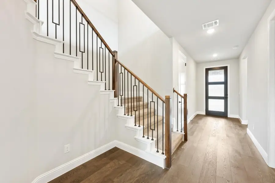 Entryway with staircase featuring iron balusters, wood handrail, and hardwood floors leading to front door Entryway with staircase featuring iron balusters, wood handrail, and hardwood floors leading to front door