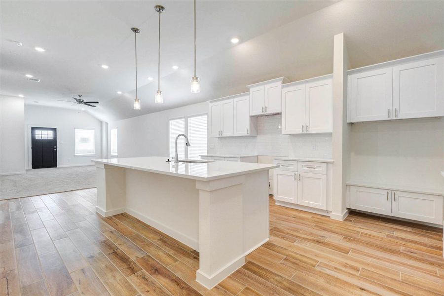 Kitchen view showcasing the oversized island, white cabinetry, quartz counters, subway tile backsplash, pendant lighting, and open connection to the living room. The layout is designed for easy entertaining and comfortable everyday living.