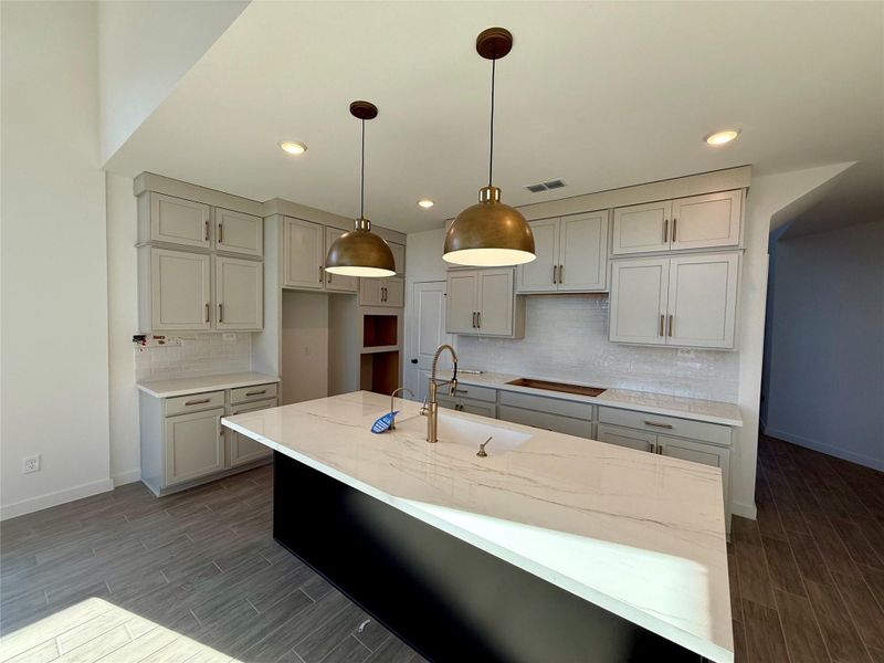 Luxurious kitchen features stacked cabinets that reach the ceiling, offering both beauty and abundant storage. Quartz countertops gleam beneath elegant pendant lighting, creating a space that feels modern and inviting.