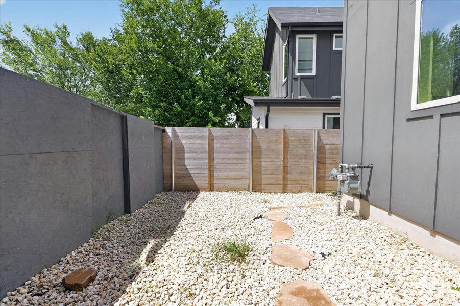 A private yard features gravel landscaping, stepping stones, and a sturdy privacy fence.