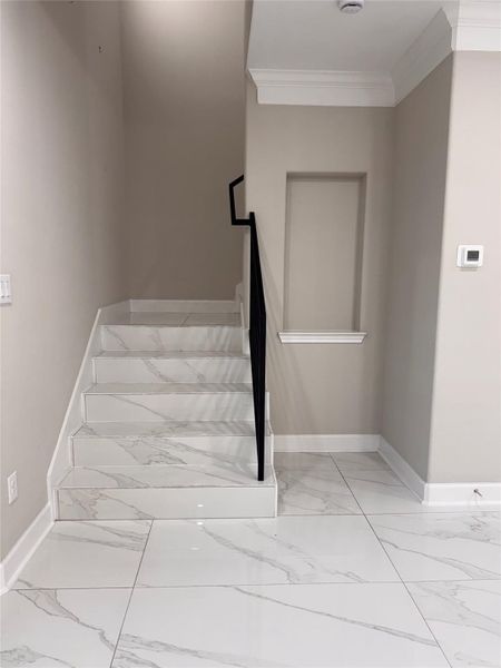 Elegant staircase with sleek marble flooring and a modern black handrail, set against a neutral-toned wall with stylish recessed shelving. Elegant staircase with sleek marble flooring and a modern black handrail, set against a neutral-toned wall with stylish recessed shelving.