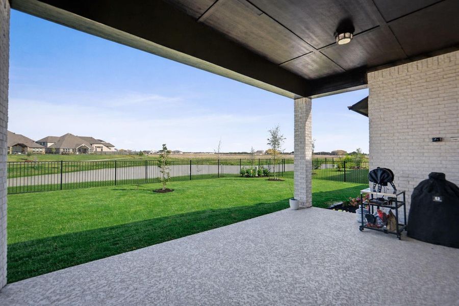 Expansive lawn with wrought-iron fencing offers unobstructed views of the community water feature. The covered patio provides an ideal space for outdoor relaxation during golden hour.