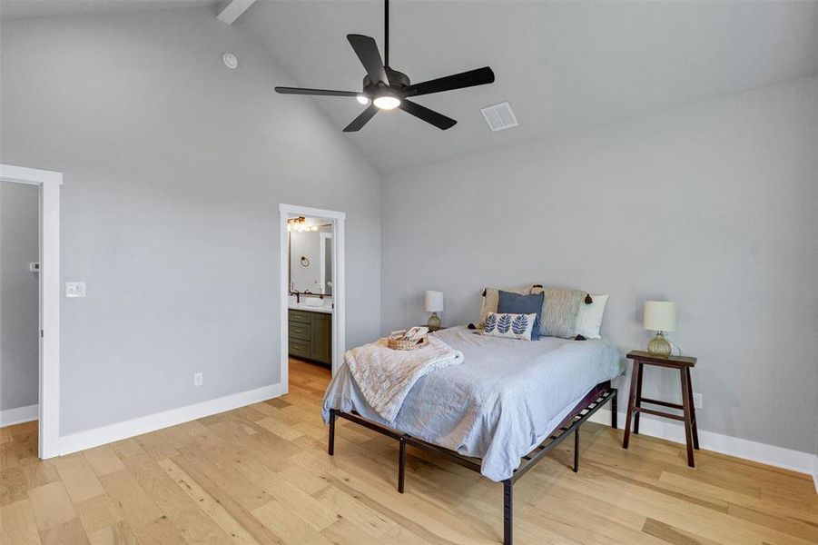 Bedroom featuring high vaulted ceiling, light wood-style flooring, beam ceiling, ceiling fan, and connected bathroom Bedroom featuring high vaulted ceiling, light wood-style flooring, beam ceiling, ceiling fan, and connected bathroom