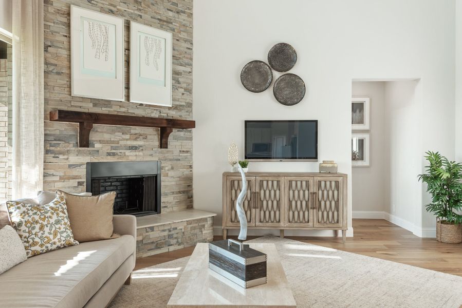 Living room with stacked stone fireplace, wood mantel, hardwood floors, and wall-mounted TV on a media console