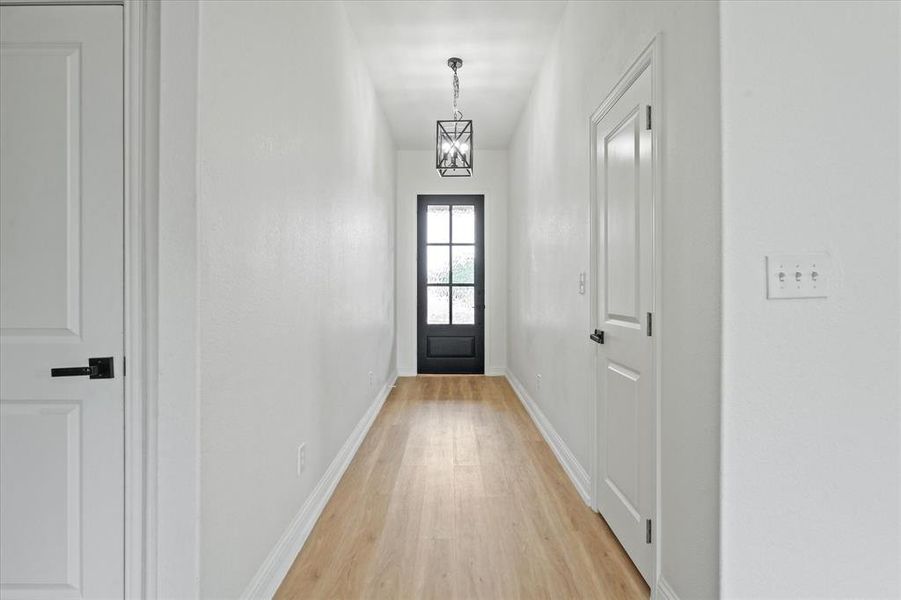 Hallway featuring wood-finish flooring, recessed doors with black hardware, a black paneled door with glass inserts, white walls, and an overhead caged light fixture