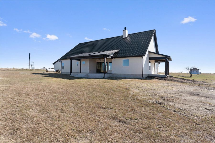 Rear view of house with a metal roof, a chimney, a patio, and a yard