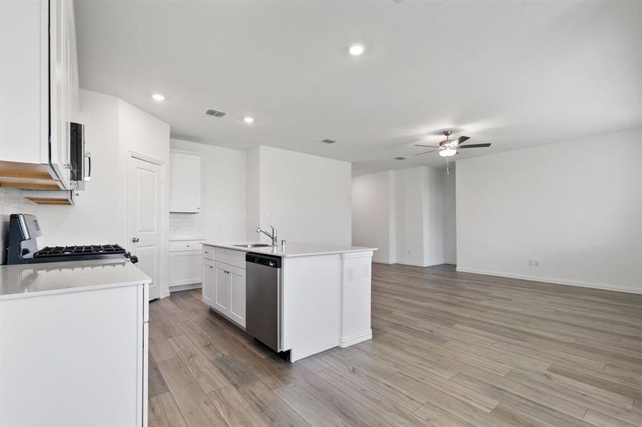 Kitchen featuring gas stove, a kitchen island with sink, white cabinets, light wood-type flooring, and dishwasher
