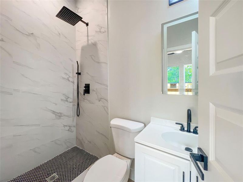 Bathroom with toilet, vanity, and a marble finish shower