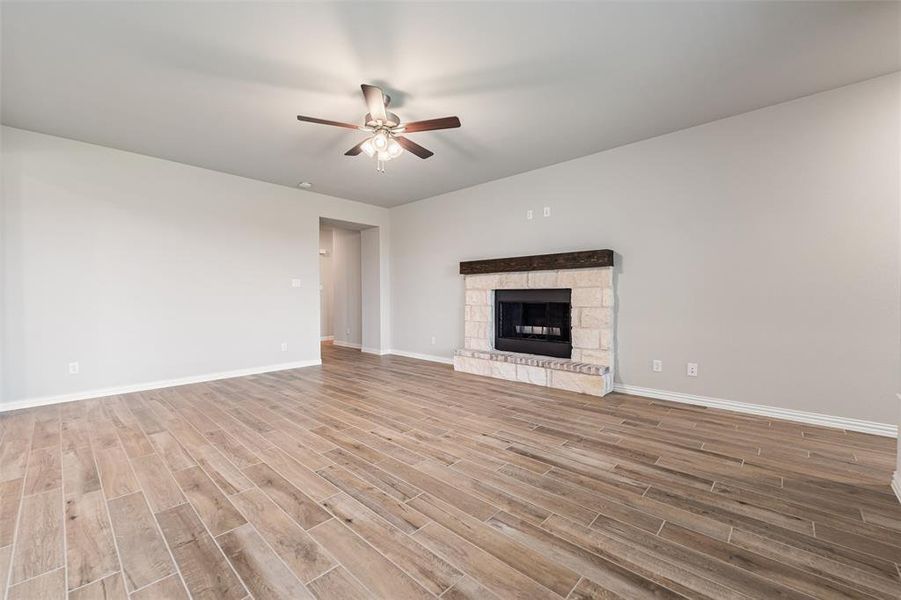 Unfurnished living room with a stone fireplace, ceiling fan, and light wood-style floors Unfurnished living room with a stone fireplace, ceiling fan, and light wood-style floors