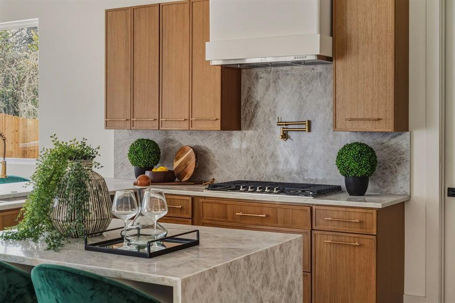 Kitchen with wall chimney exhaust hood, light stone countertops, tasteful backsplash, brown cabinets, and stainless steel gas cooktop