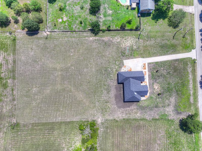 New construction with a dark gray shingle roof, concrete driveway, and surrounding land