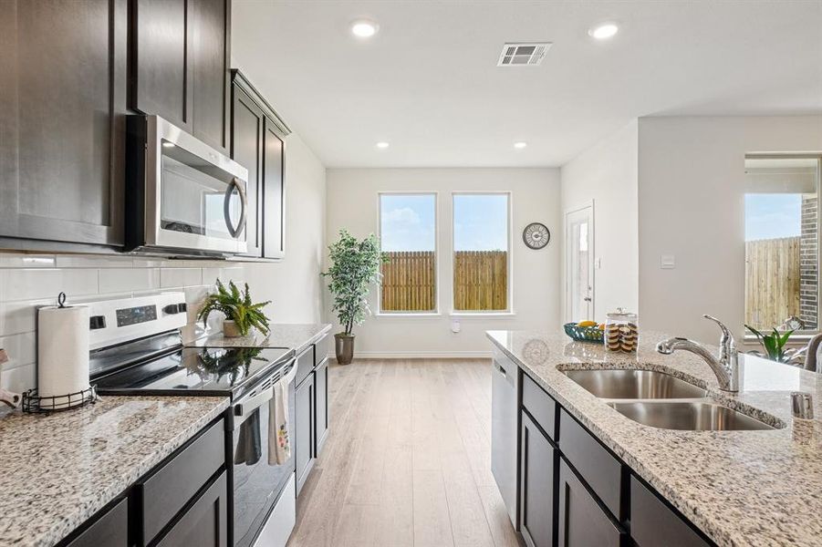 Kitchen with appliances with stainless steel finishes, light stone counters, light wood-style flooring, recessed lighting, and tasteful backsplash Kitchen with appliances with stainless steel finishes, light stone counters, light wood-style flooring, recessed lighting, and tasteful backsplash