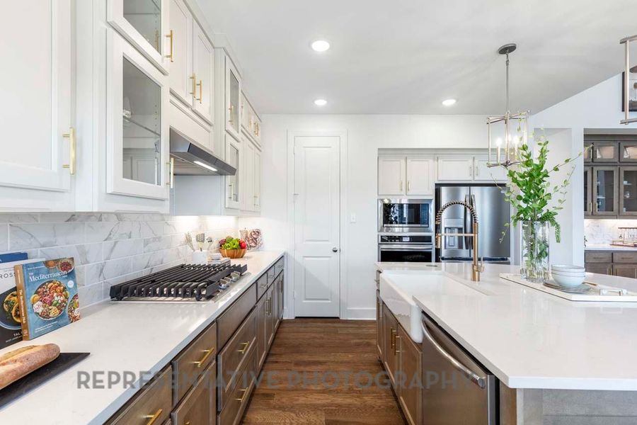 Kitchen featuring stainless steel appliances, light countertops, dark wood-type flooring, an island with sink, and white cabinetry Kitchen featuring stainless steel appliances, light countertops, dark wood-type flooring, an island with sink, and white cabinetry