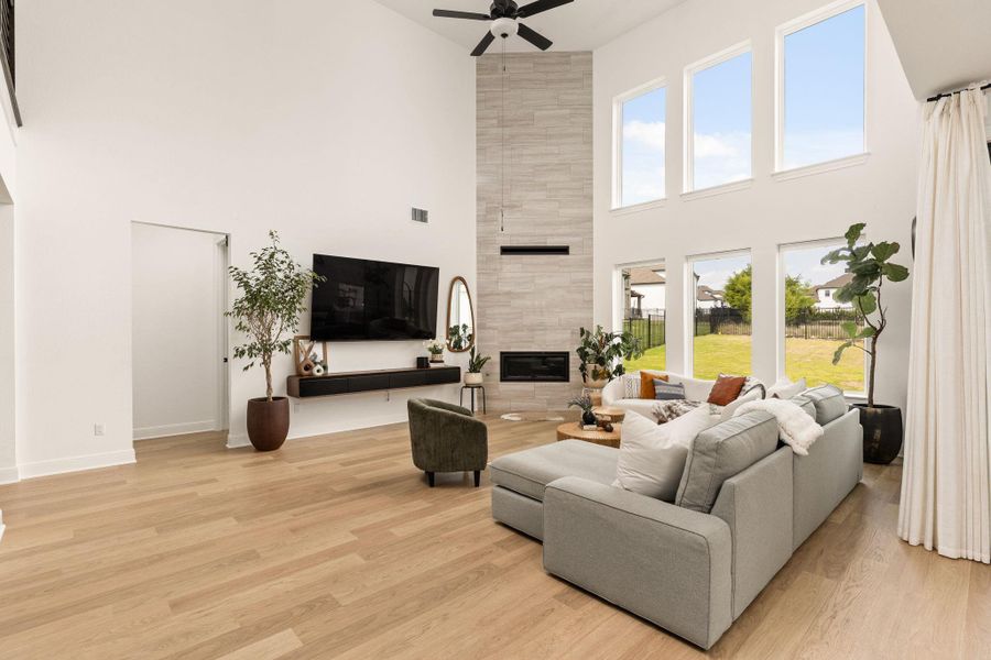 Vaulted ceiling living area featuring wood-finish flooring, a contemporary fireplace with a stone surround, and a ceiling fan