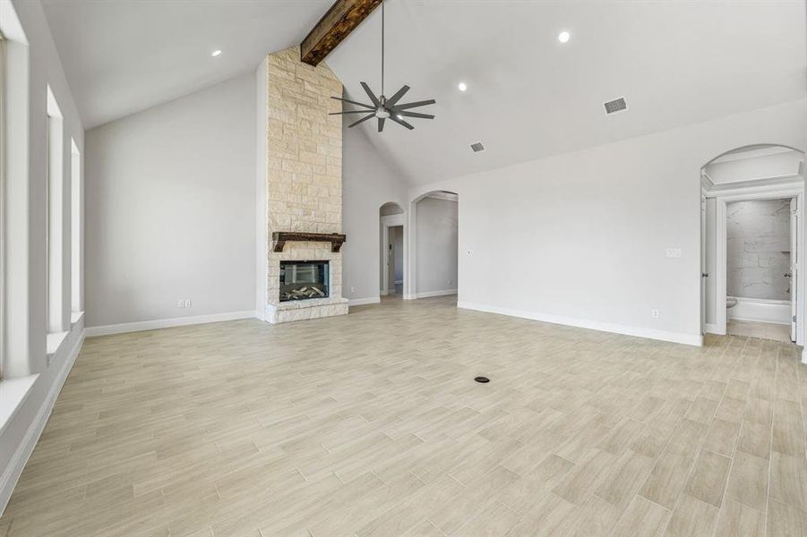 Unfurnished living room with beam ceiling, arched walkways, ceiling fan, light wood-style flooring, and a stone fireplace