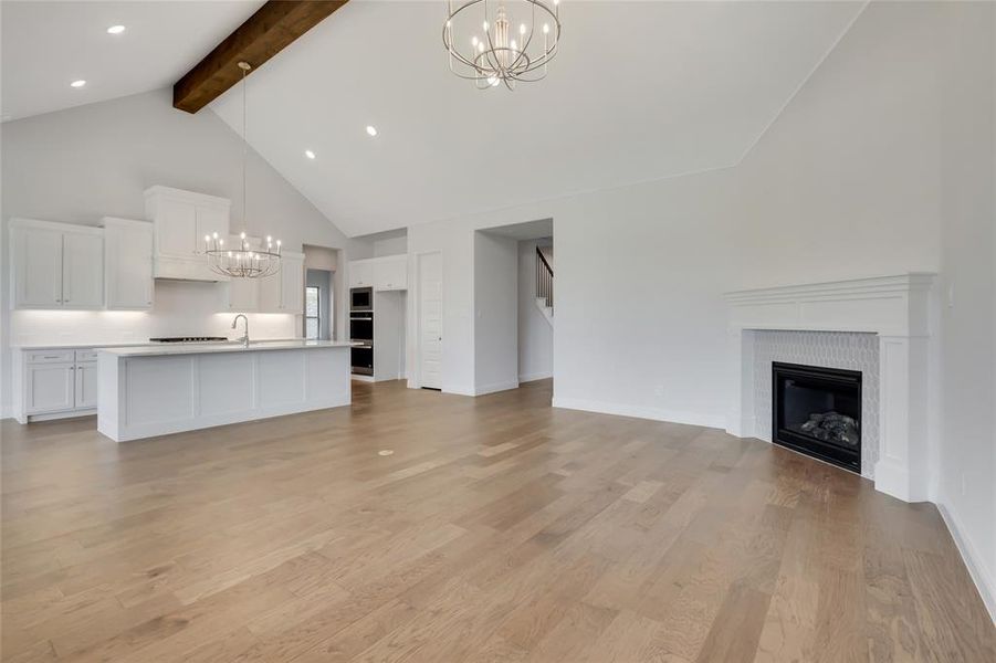 Unfurnished living room with high vaulted ceiling, an inviting chandelier, a fireplace, beamed ceiling, and light wood-type flooring