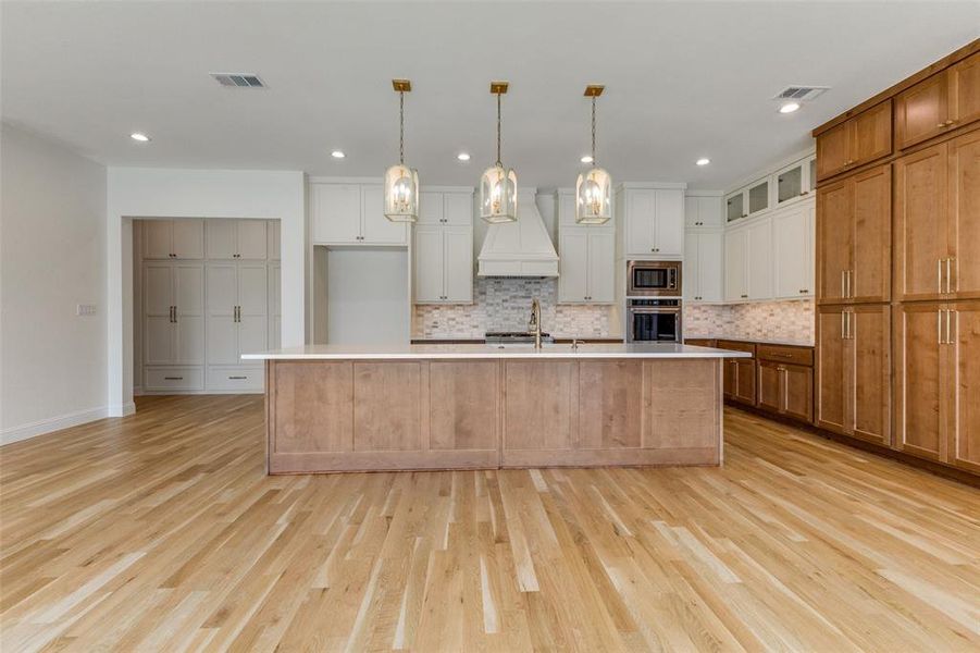 Kitchen featuring stainless steel appliances, custom exhaust hood, light wood finished floors, tasteful backsplash, and recessed lighting