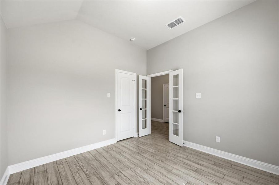 Unfurnished room featuring french doors, light wood-style floors, and vaulted ceiling Unfurnished room featuring french doors, light wood-style floors, and vaulted ceiling
