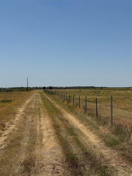 A long grassy driveway runs alongside fenced acreage under a clear blue sky.